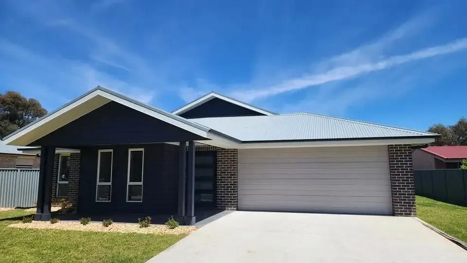 A Black House with A White Garage Door and A Blue Sky in The Background — Illawarra Garage Doors in Albion Park Rail, NSW