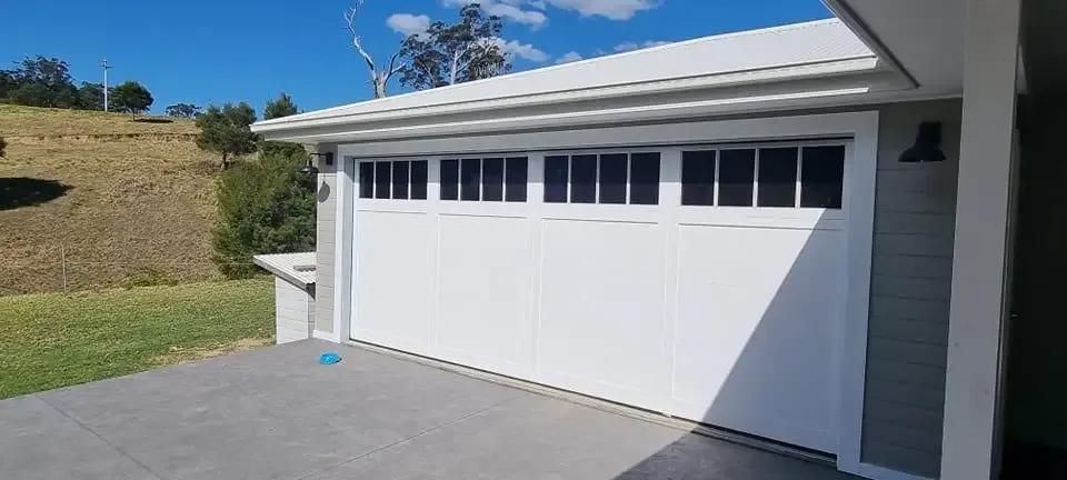 A Large Wooden Garage Door Is Sitting in Front of A Brick Building — Illawarra Garage Doors in Nowra, NSW
