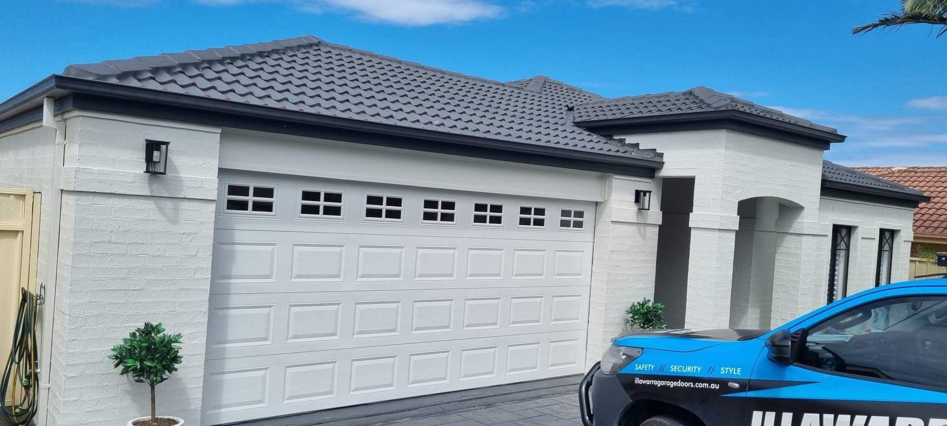 A Blue Car Is Parked in Front of A White House — Illawarra Garage Doors in Albion Park Rail, NSW