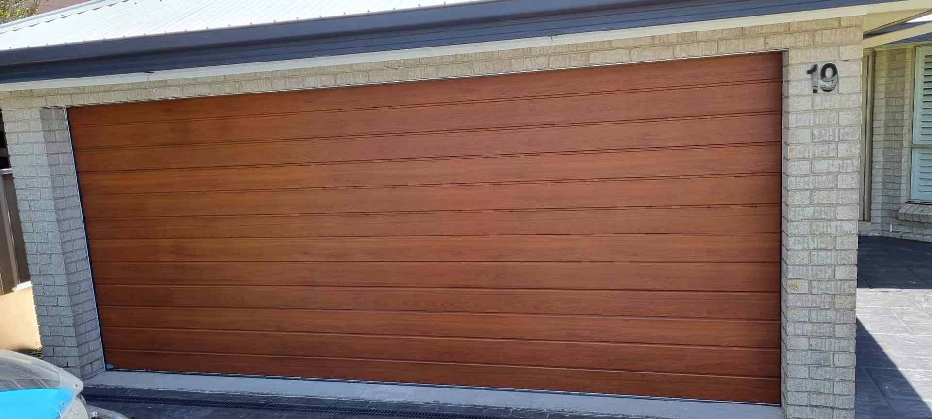 A Wooden Garage Door Is Sitting in Front of A Brick Building — Illawarra Garage Doors in Albion Park Rail, NSW