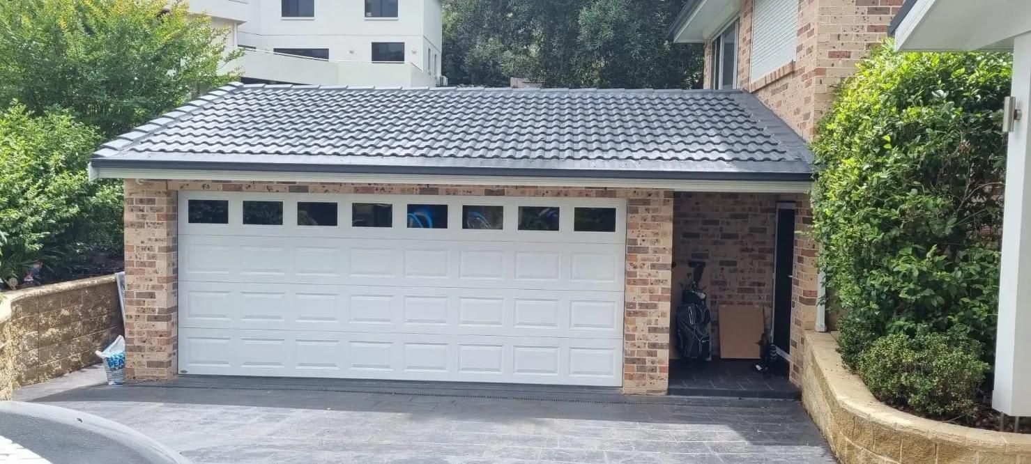 A White Garage Door Is Sitting in Front of A Brick House — Illawarra Garage Doors in Albion Park Rail, NSW