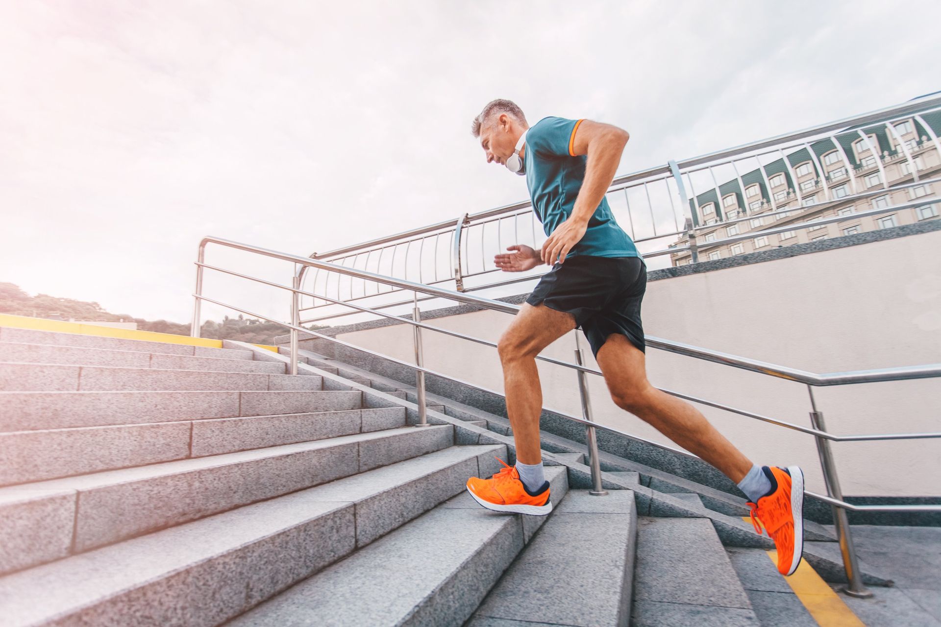 Man running up outdoor stone steps, wearing teal shirt, black shorts, and orange shoes.