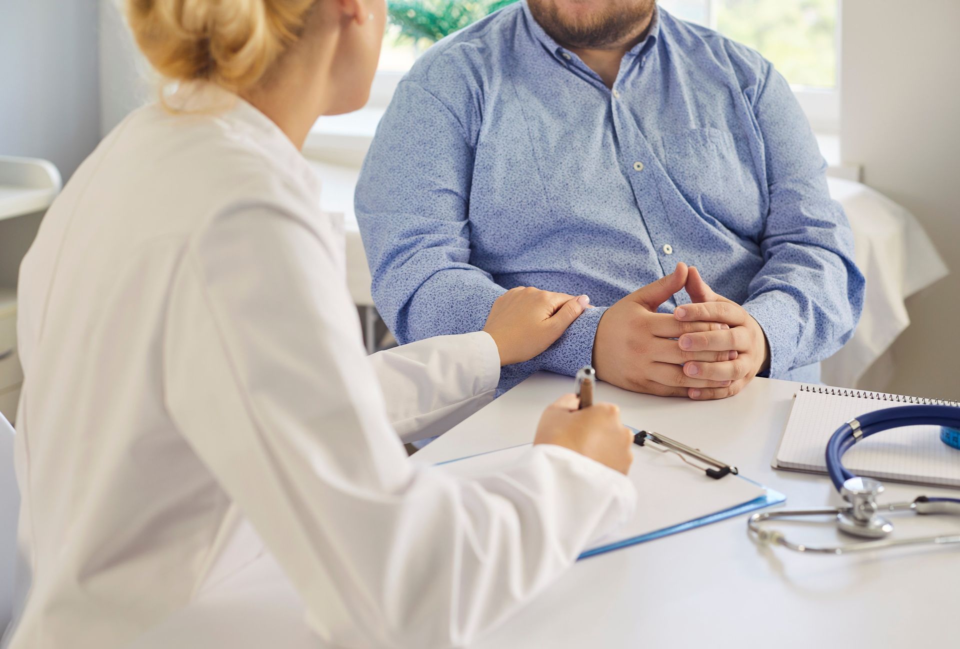 Doctor speaking with a seated patient at a desk in a bright clinic office