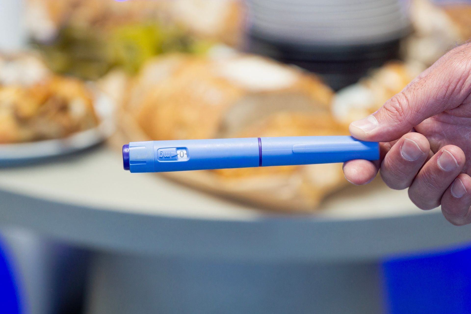 Hand holding a blue pen-like device in front of a blurred table with food plates