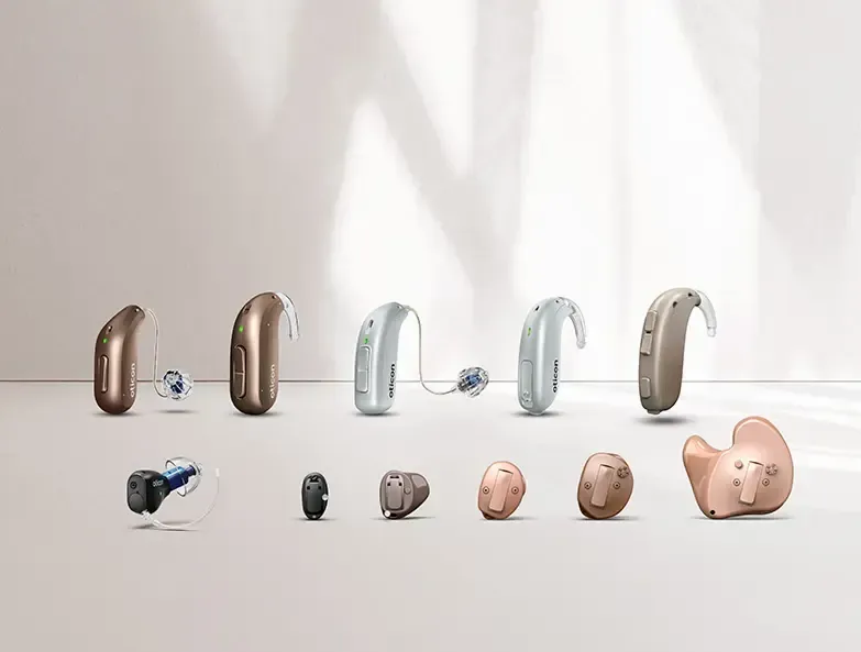 Assorted hearing aids in metallic and skin-tone colors displayed on a white surface against a light background