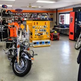 Motorcycles in a garage showroom with tool cabinets, a bright yellow display, and a red vending machine