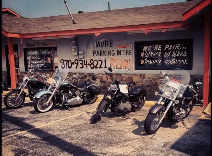 Four motorcycles parked outside a rustic shop with hand-painted signs and a phone number on the wall