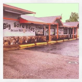 Big Bore Bikes storefront with covered walkway and stone base on a wet, overcast day