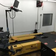 Industrial room with a yellow machine, mounted camera, and monitor on a wall.