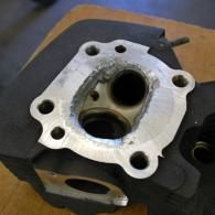 Close-up of a metal engine cylinder head with valve ports and bolt holes on a workbench