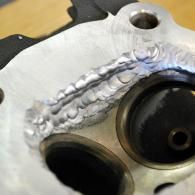 Close-up of a welded metal plate with two circular openings and a black gasket or bearing.
