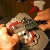 Hands using calipers to measure a metal mechanical part with red markings