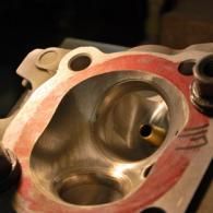 Close-up of a metal engine cylinder head with red gasket residue and two valve ports