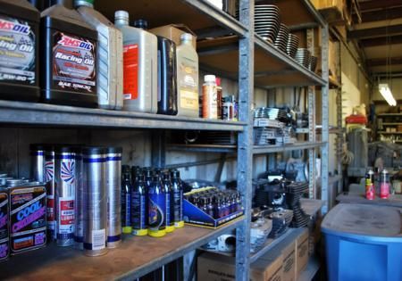 Shelves in a workshop stocked with cans, bottles, and tools beside a blue bin