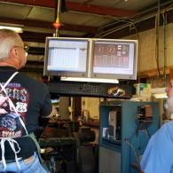 Two people view dual monitors in an industrial workshop or machine shop