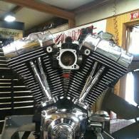 Chrome V-twin motorcycle engine displayed indoors, with polished metal fins and a central intake opening.