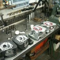 Engine cylinder heads on a factory workbench with machine parts and tooling in the background