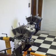 Close-up of a chrome V-twin engine mounted on a stand in a workshop with a checkered floor.