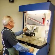 Man using a lab machine with a black part inside, in a blue industrial enclosure.
