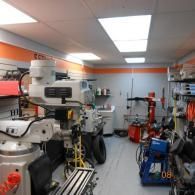 Industrial workshop with machinery, tools, and equipment along both sides of a narrow aisle.