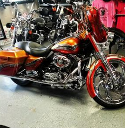 Orange and chrome cruiser motorcycle on display in a showroom with other bikes and pink shirts nearby