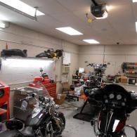 Motorcycle workshop with several bikes, a red tool chest, and overhead lights