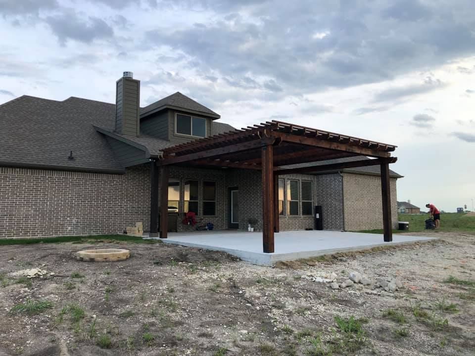 Covered patio with wooden pergola beside a brick house under a cloudy sky