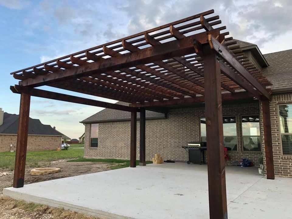 Wooden pergola over a concrete patio beside a brick house in a suburban backyard