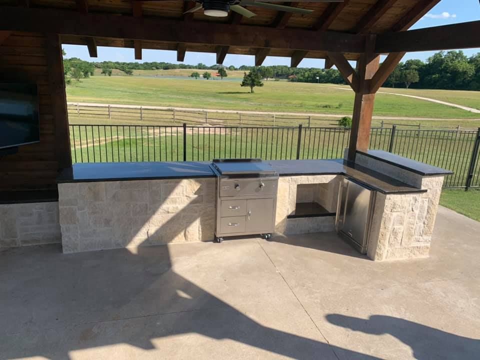 Outdoor pavilion with stone counter and sink overlooking a grassy field