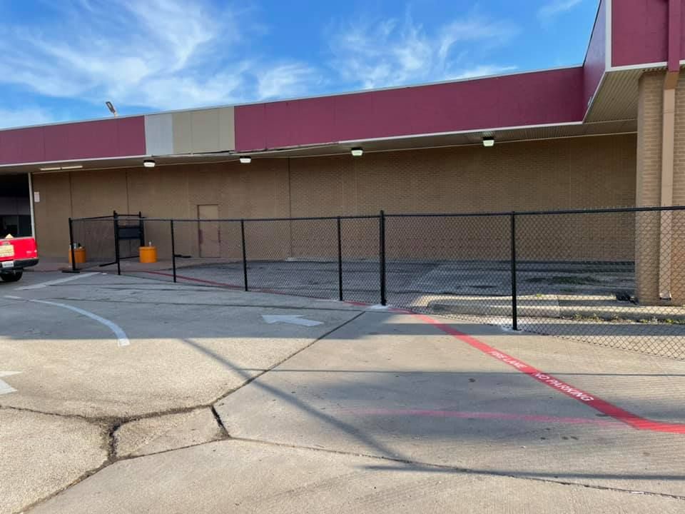 Closed storefront with a black chain-link fence across the front and cracked pavement in a parking lot.
