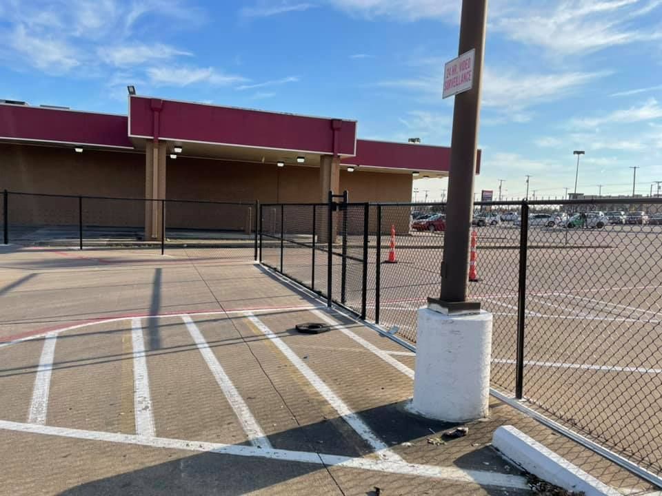 Empty parking lot with chain-link fence, white accessibility lines, and a maroon building in the background