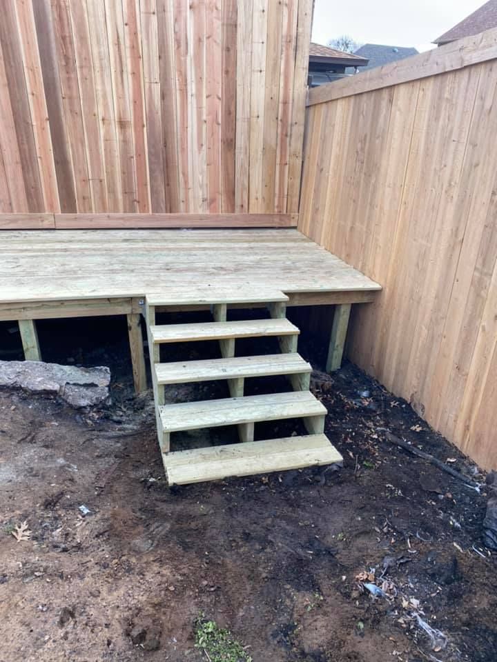 Small wooden deck with stairs in a fenced dirt backyard construction area