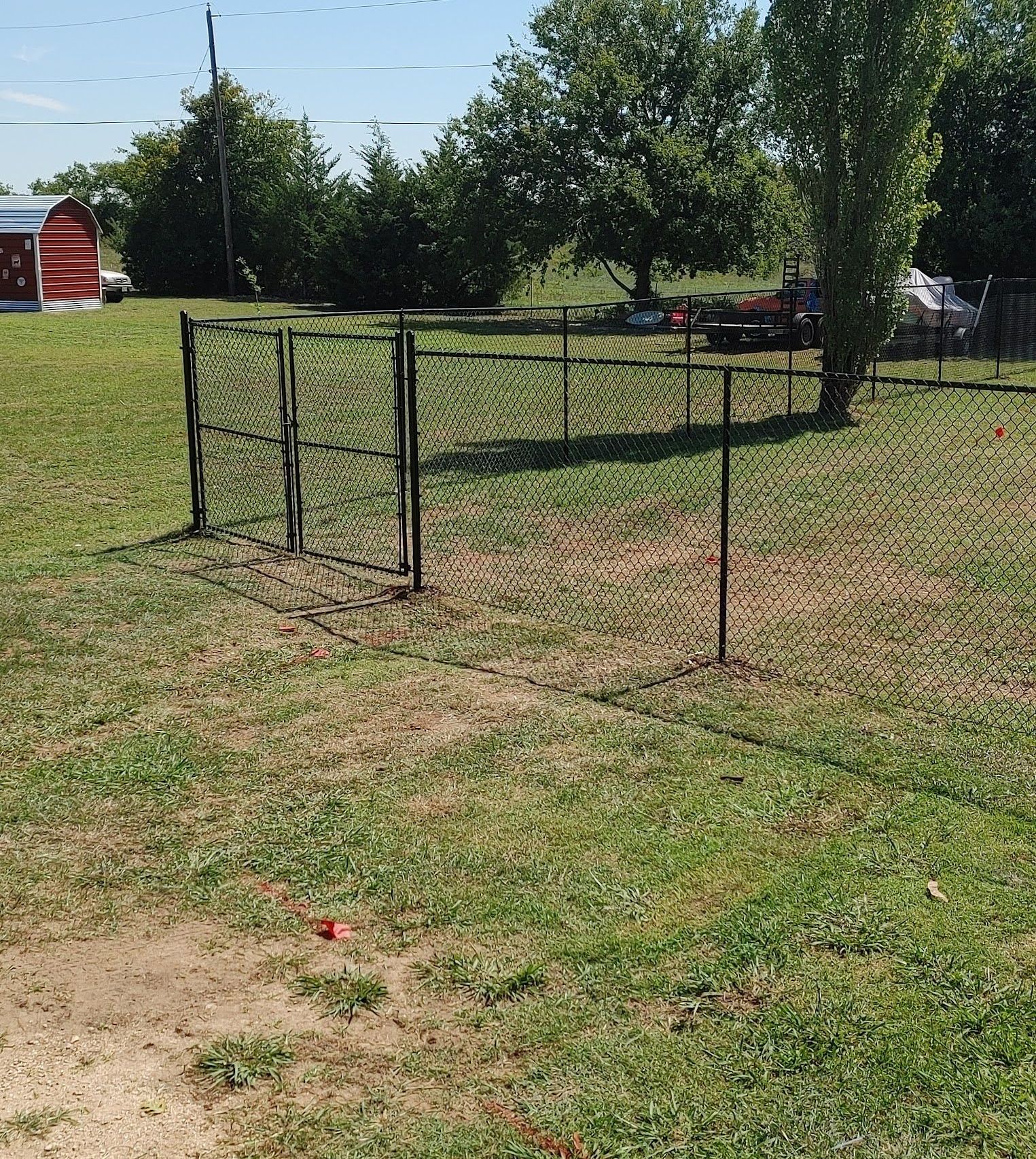 Small black metal pen in a grassy backyard with trees and a red shed in the background