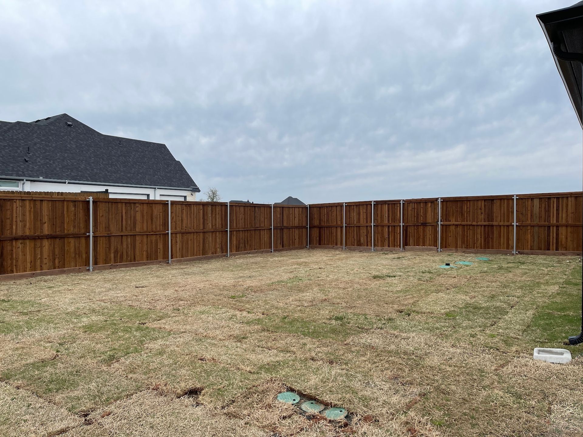Empty fenced backyard with brown wooden privacy fence under a cloudy sky