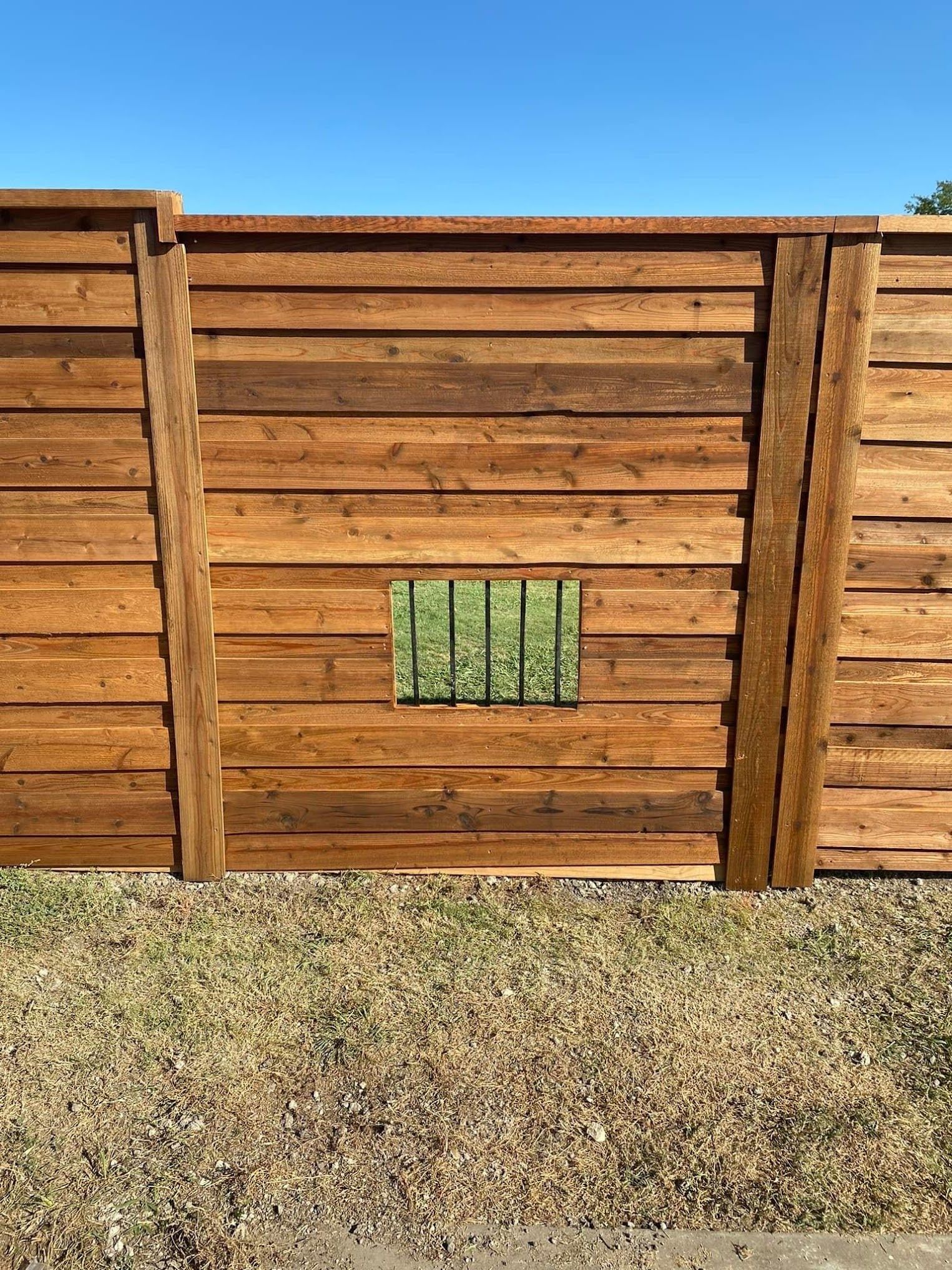 Wooden fence with a small green barred window and gravel ground in front