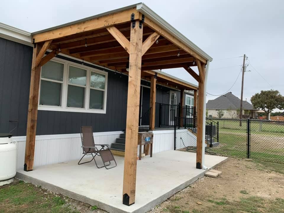 Wooden porch shelter attached to a house with a chair, overcast yard, and chain-link fence nearby