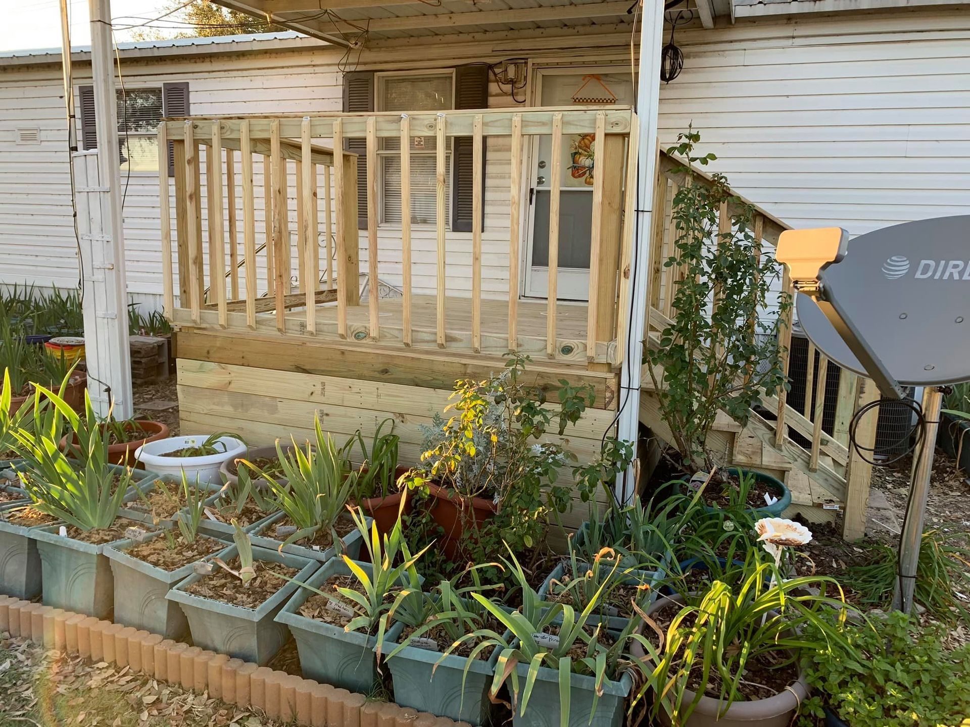 Small front porch under construction beside a flower bed and satellite dish