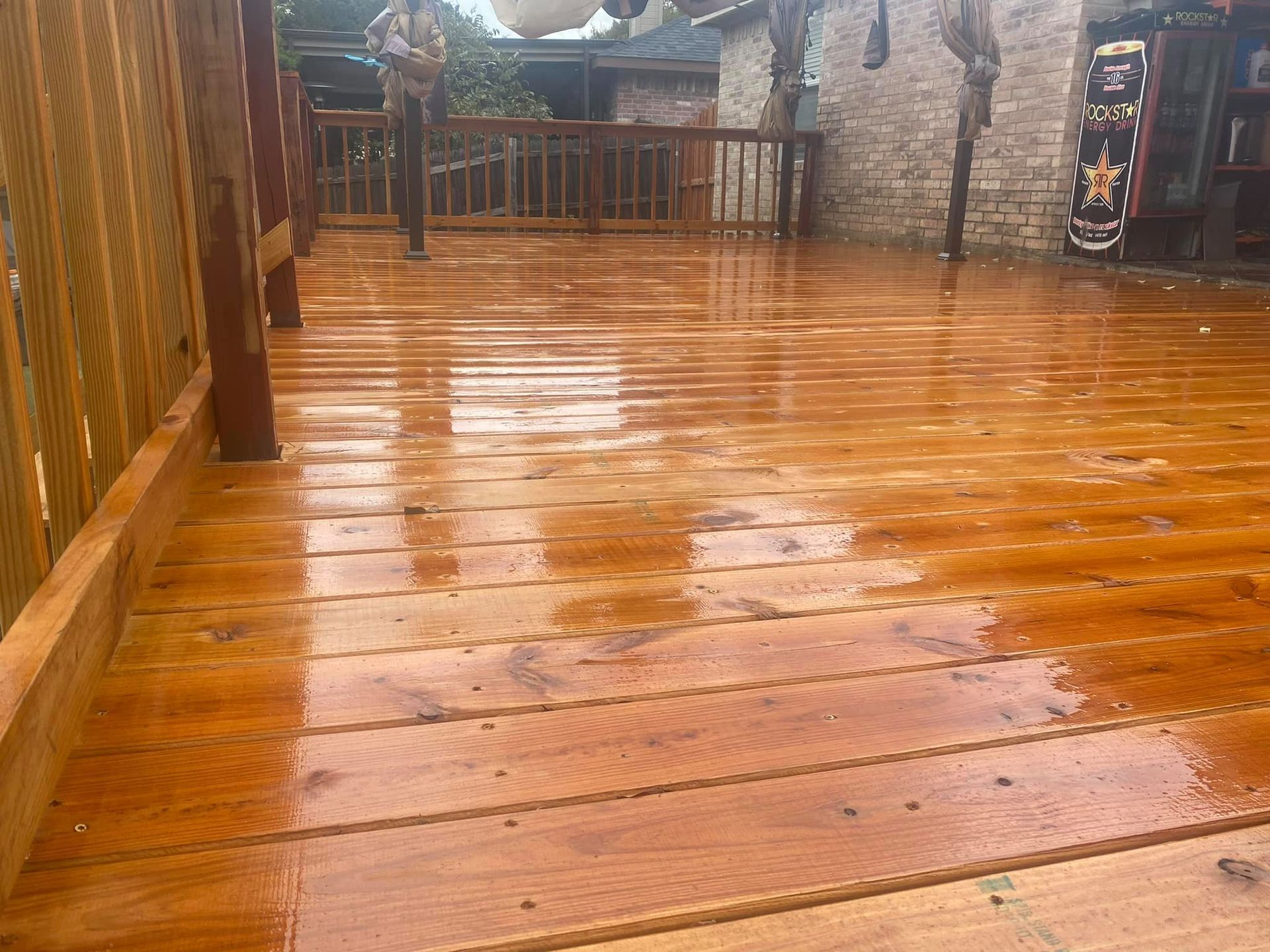 Wet wooden boardwalk with raindrops, leading toward a rustic outdoor building and fence.