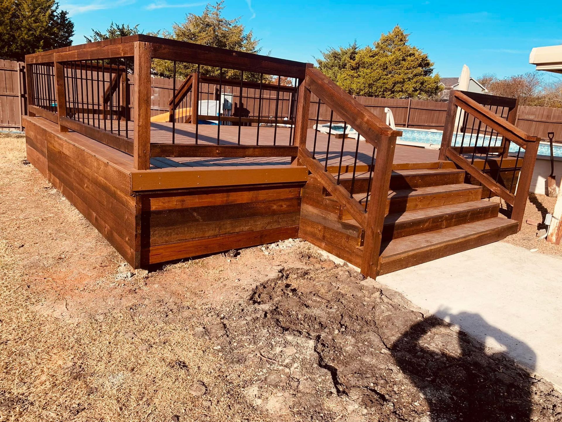 Brown wooden deck with stairs and railings in a sunny backyard on dry ground