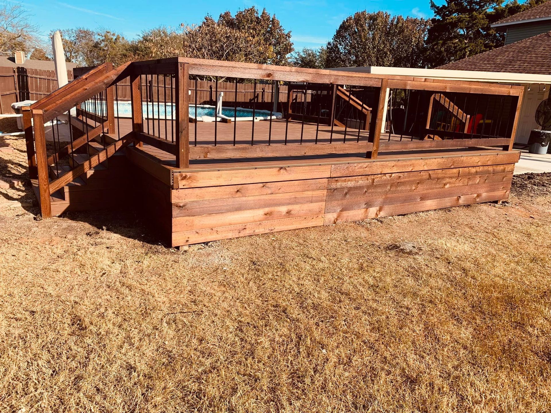 Wooden deck with railings and ramp on a dry grassy yard under a clear sky