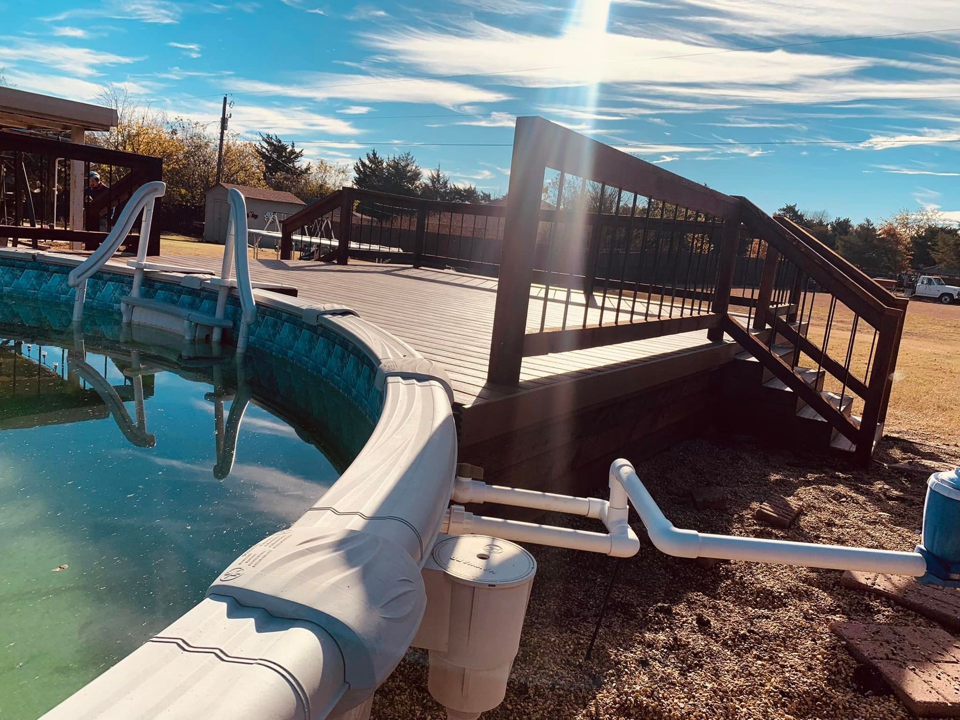 Outdoor pool with a curved white slide and wooden deck under a bright blue sky