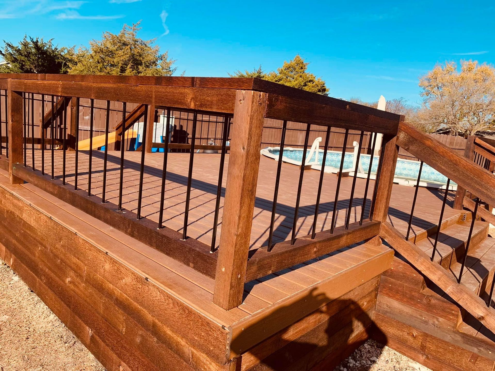 Wooden deck railing with black metal balusters in a sunny outdoor setting