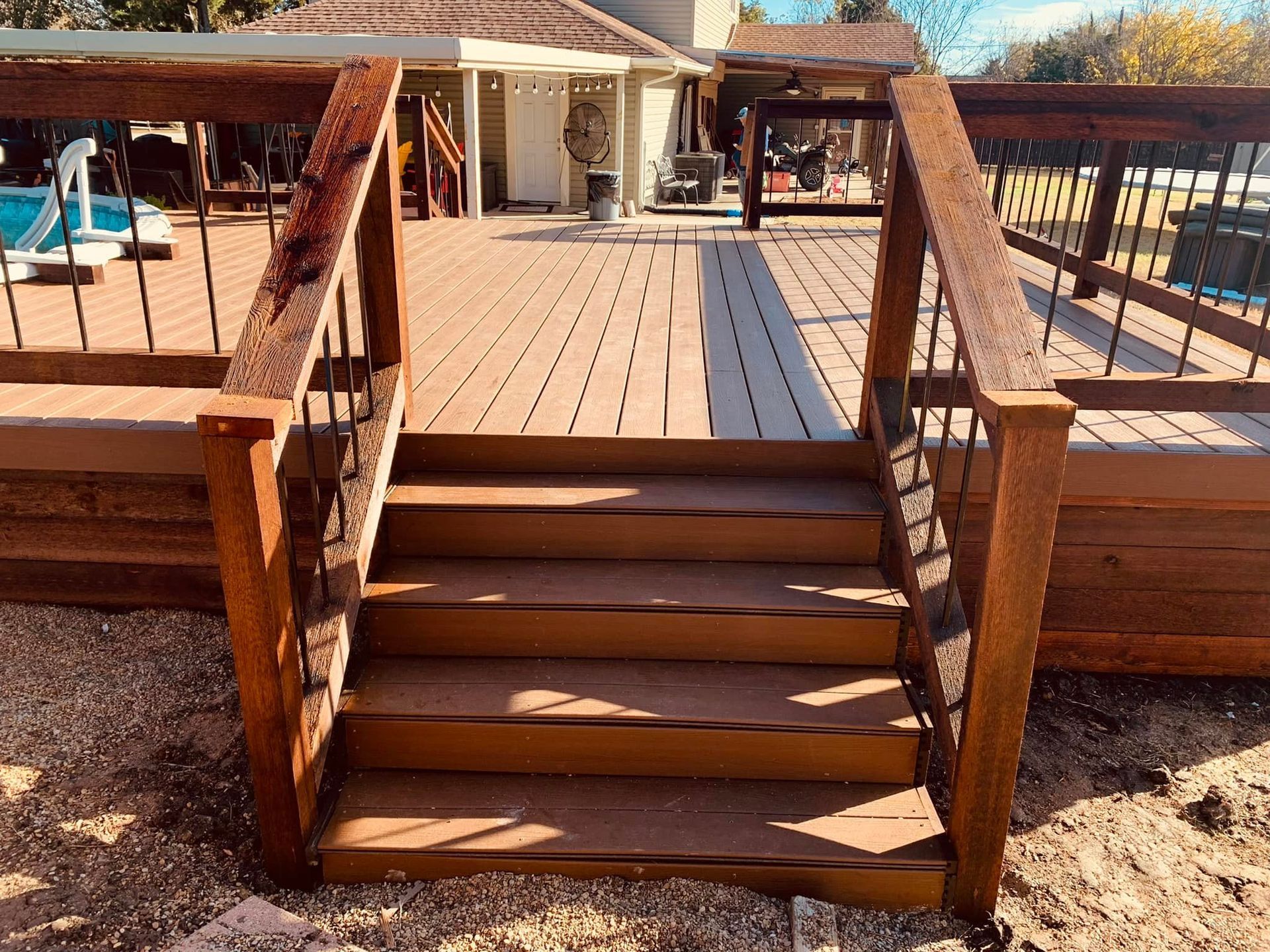 Wooden deck with short stairs and railings leading to a sunlit outdoor patio