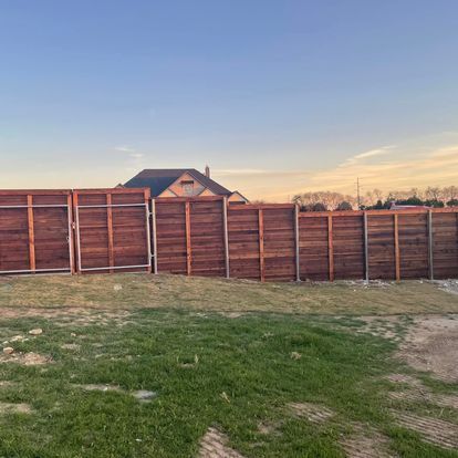 Wooden backyard fence at sunset with grass and a house roof in the background