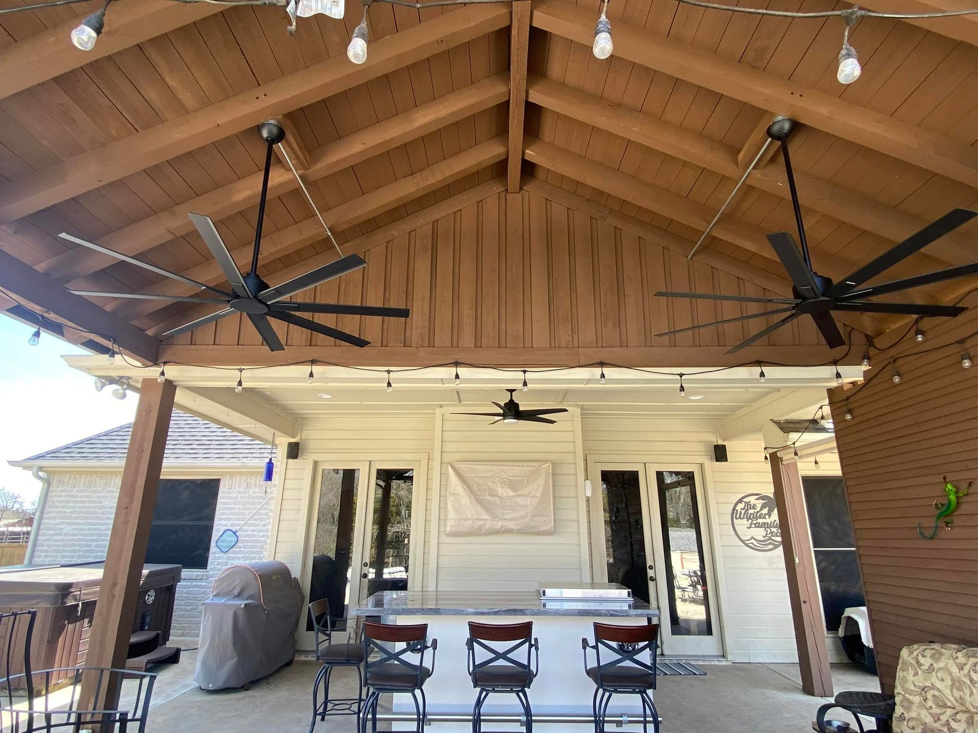 Covered patio with wood ceiling, two ceiling fans, string lights, and outdoor seating around a table.