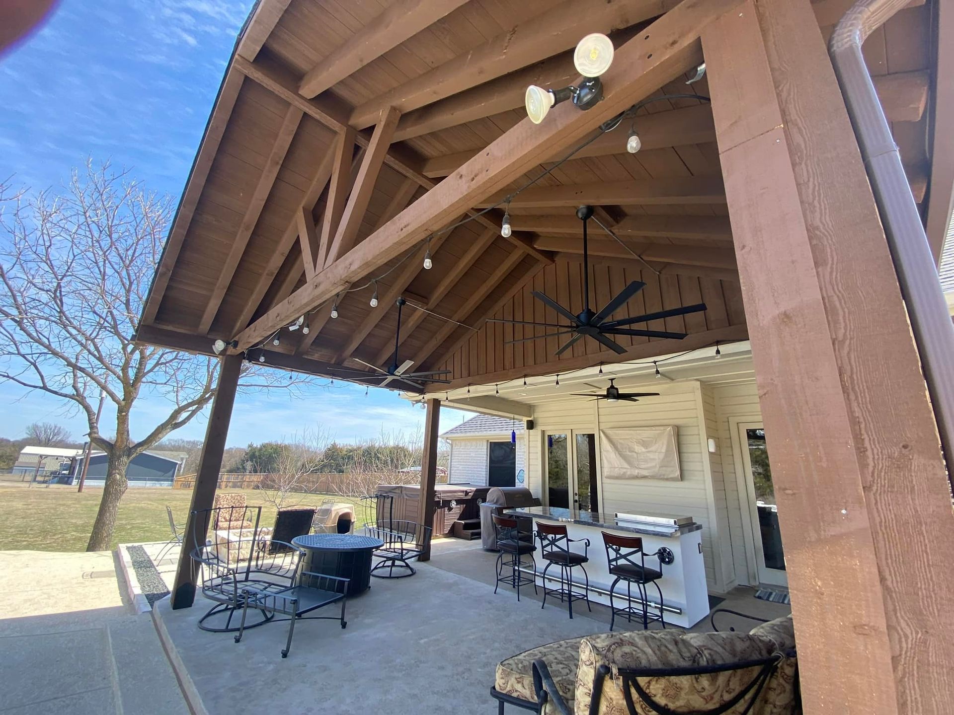 Covered patio with ceiling fans, tables and chairs, and a grill in a backyard setting
