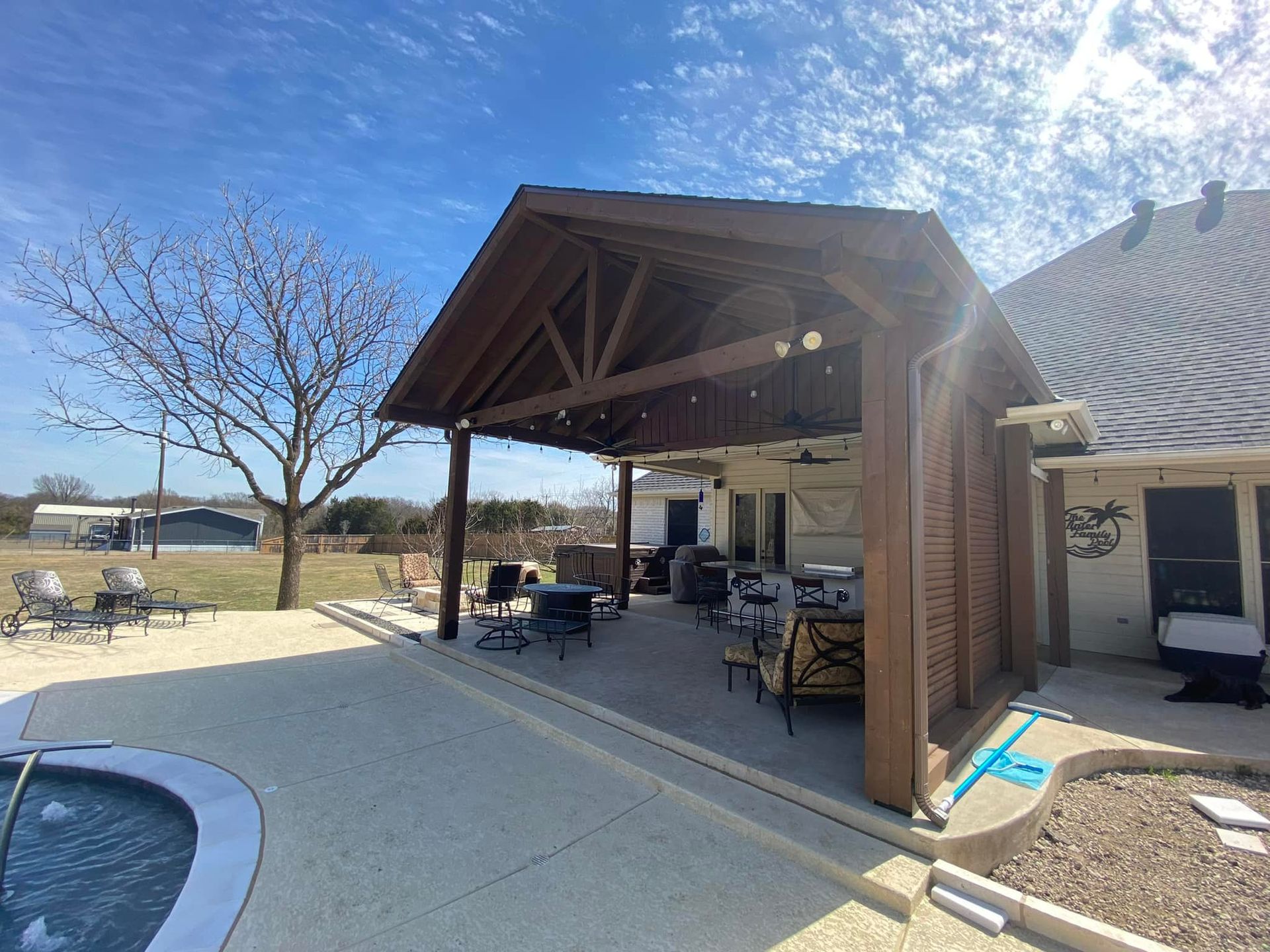 Covered patio beside a pool, with outdoor seating and sunlight in a backyard setting