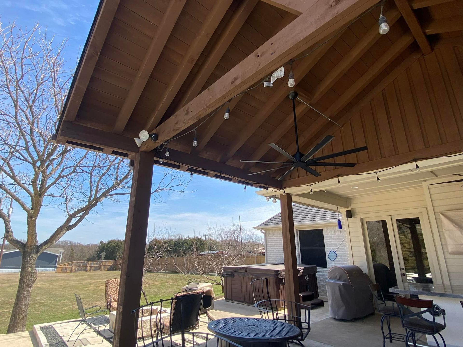Covered patio with wooden roof, ceiling fan, outdoor furniture, and grassy yard beyond