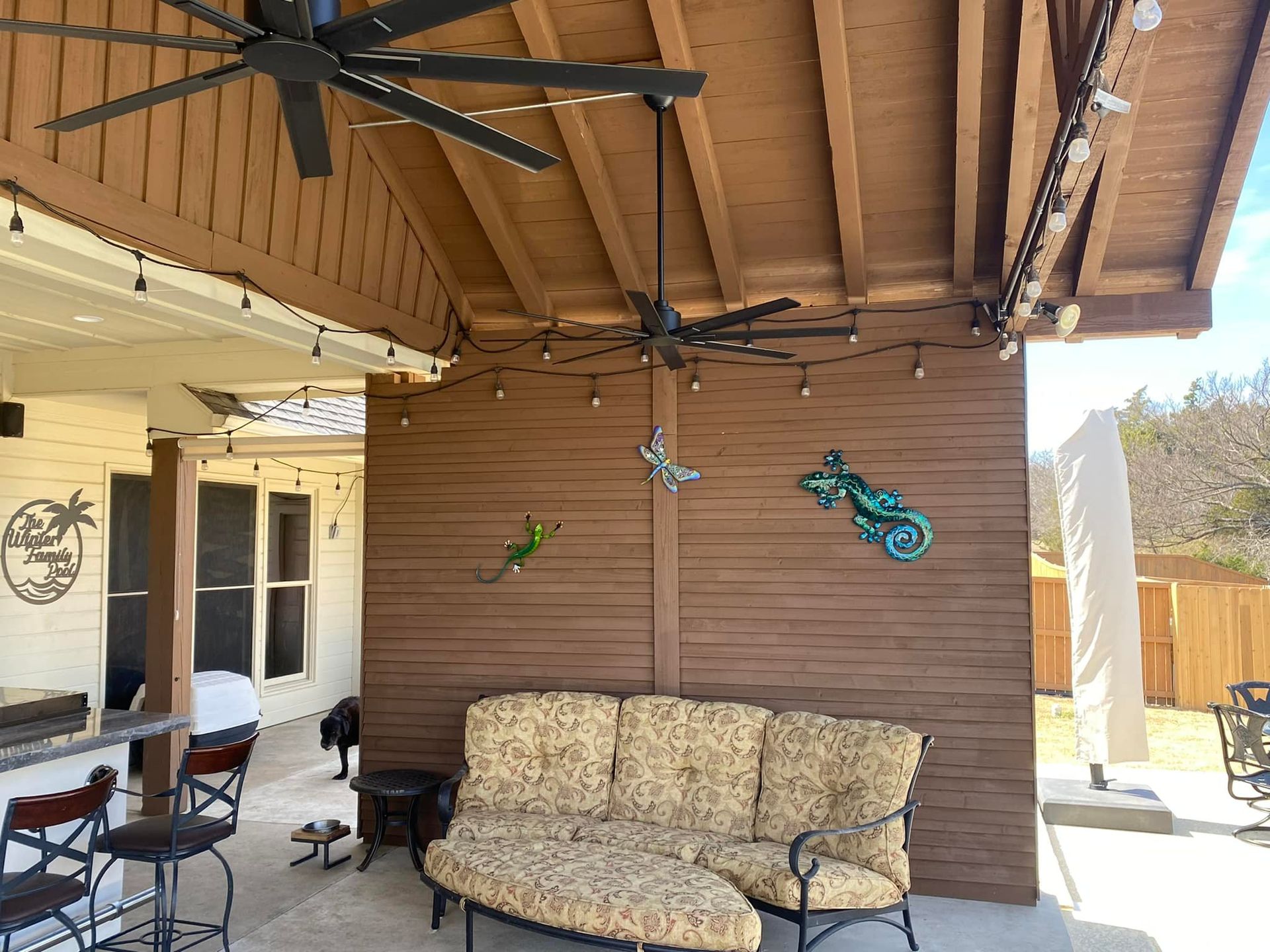 Patio with brown wood wall, patterned couch, ceiling fans, and hanging butterfly decorations under a covered roof