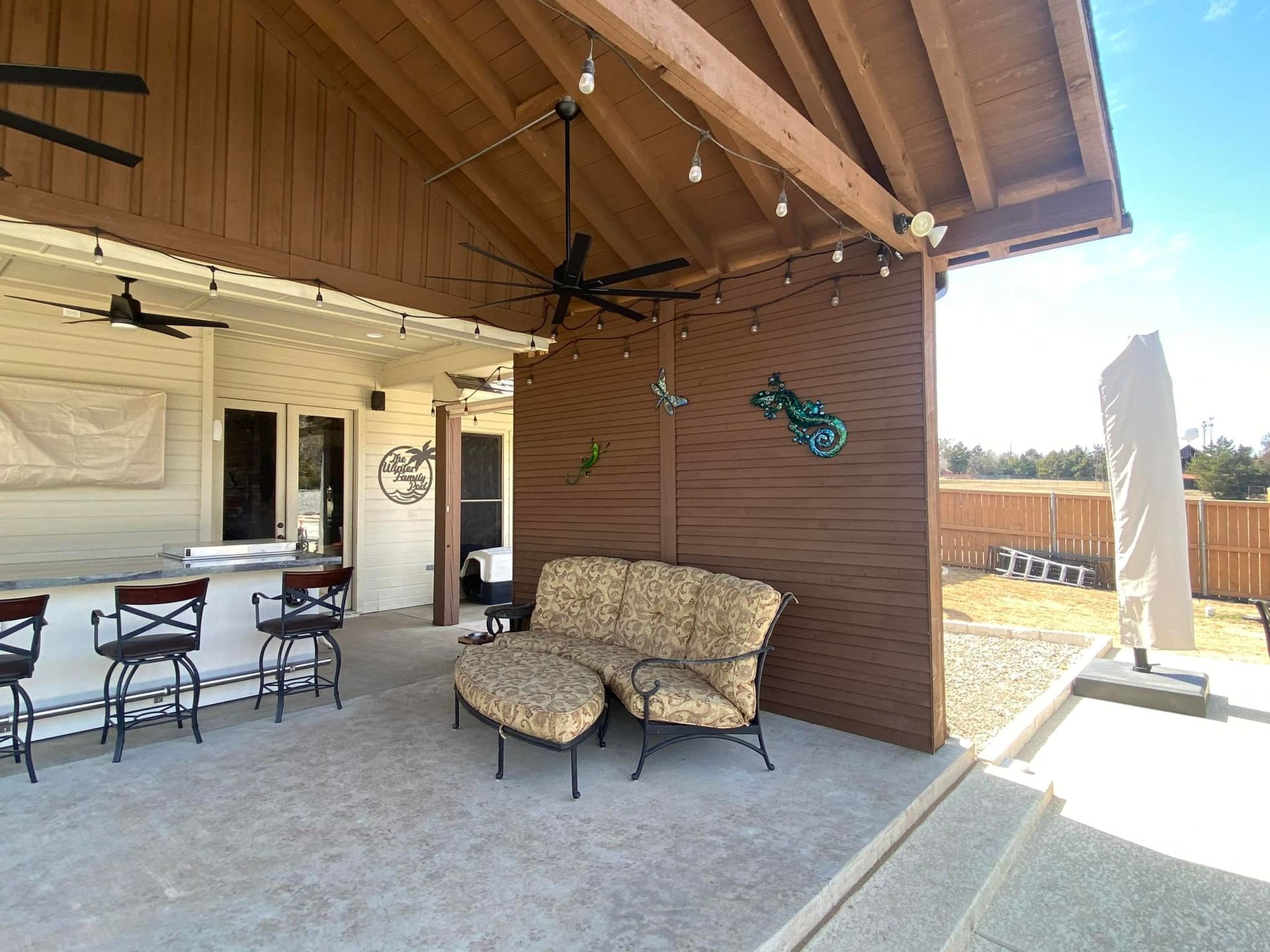 Covered patio with wicker loveseat, outdoor table and chairs, and a brick wall with decor